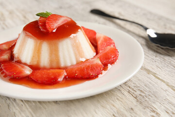 Delicious panna cotta with strawberry and mint in plate on light wooden background, closeup