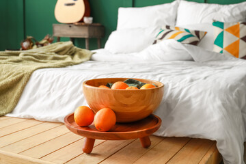 Wooden bowl with oranges near comfortable bed with soft linens