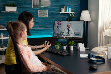 Woried parent holding pills bottle discussing medicine treatment against daughter sickness with remote physician during online videocall meeting conference. Distance medical consultation