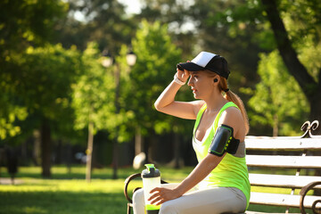 Sporty mature woman with bottle of water sitting on bench in park