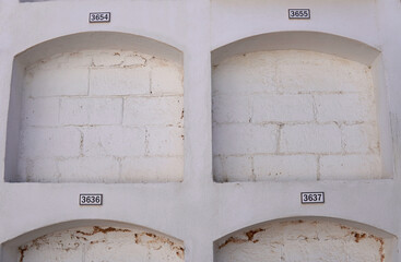 Empty cemetery niches, numbered and painted white with exposed brick
 