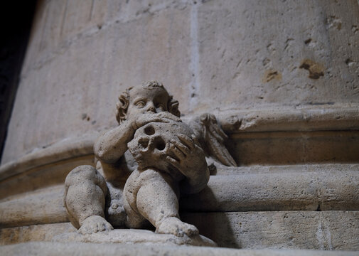 Stone sculpture next to a column, in Gothic style, of a naked child with a skull in his arms