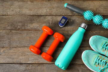 Pulse oximeter, bottle of water, shoes and sport equipment on wooden background