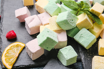 Board with tasty sweet marshmallows, mint and fruits on dark background