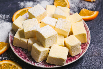 Plate with tasty sweet marshmallows and orange on dark background