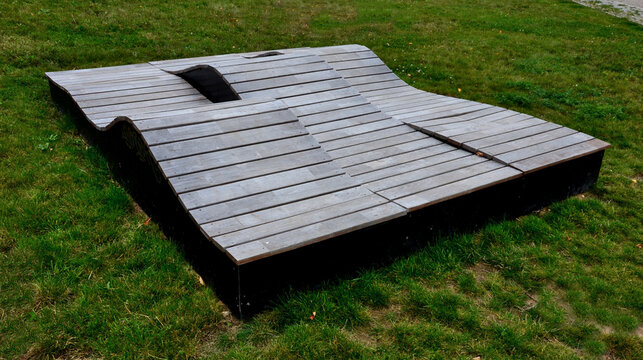 deck chair composed of three waves which are made of wood and board. large seating elements in a landscape park. furniture for tenagers
