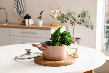 Fototapeta na wymiar Copper cooking pot with fresh spinach on table in kitchen