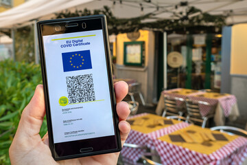 Woman showing on smartphone EU Digital Covid Certificate Green Pass with quad code. Restaurant...