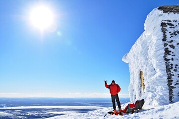 Alpinist standing near forsaken ski lift station with travel backpacks in front of huge snow capped...