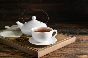 Wooden board with cup of tasty hojicha green tea and pot on table
