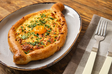 Plate with tasty Ajarian khachapuri on wooden background