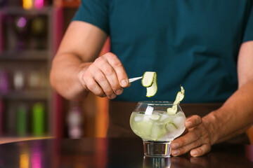 Male bartender making cucumber gin and tonic on table in bar