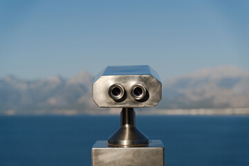 coin operated binoculars in front of mountains and sea
