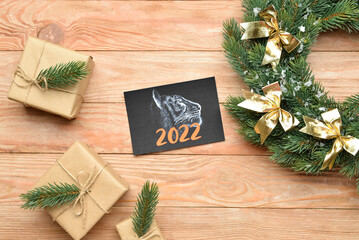 Greeting card for New Year 2022 celebration with gifts and wreath on wooden background