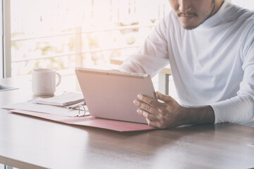 Asian businessman who sitting work by tablet in feeling happy at the office with daylight from window and blur garden background.