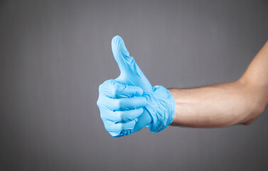 Hand in medical glove making thumb up gesture.