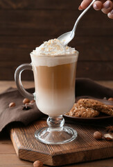 Glass cup of tasty latte with nuts on wooden background