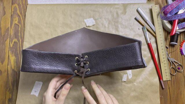 Women's hands tie lacing on corset made of leather and eva foam. Dragon belt for viking or celtic costume. Cosplayer is preparing for festival or performance.