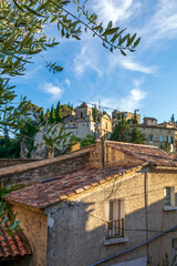 Fototapeta premium Vaison-la-Romaine street view on medieval upper village with red roofs, green trees and blue sky, Provence, France