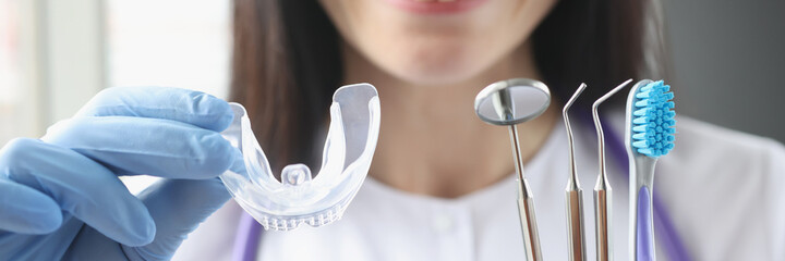 Smiling female doctor holds transparent plastic mouth guard and stomatological instruments in her...