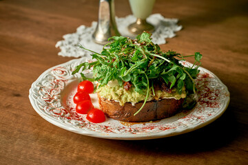 Appetizing toast sandwich: bread, avocado, cream cheese, mini mozzarella, sun-dried tomatoes, arugula, microgreen.