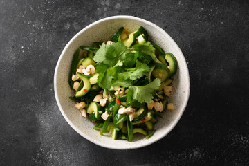 Asian Broken Cucumber salad with fresh coriander, ginger, chili pepper, black vinegar in white bowl isolated on black background. Spicy cucumbers. Popular Chinese vegetable appetizer. Top view.
