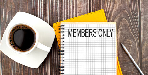 MEMBERS ONLY text on the notebook with coffee on wooden background