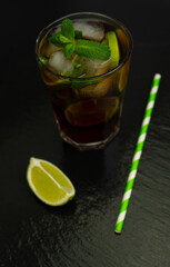 Cuba Libre cocktail with brown rum, lemon juice, coke and ice cubes, decorated with fresh lime slice on modern black stone tray