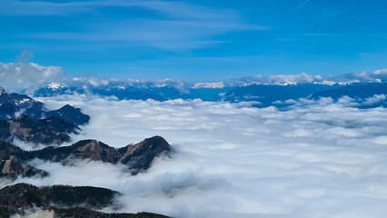 A panoramic view from the top of Alpine peak in Austria. The whole area is shrouded in thick clouds. A few peaks popping out from the clouds. High mountain chains in the back. Carpet from the clouds