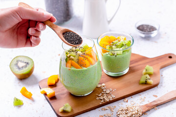 Woman adding chia seeds to matcha and fruits pudding