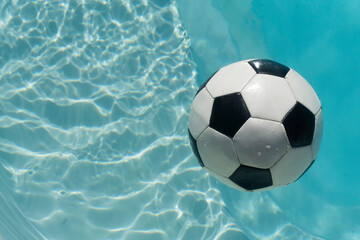 Fototapeta na wymiar Black and white soccer football floating in a blue clear swimming pool. Summer sport background