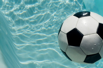 Black and white soccer football floating in a blue clear swimming pool. Summer sport background