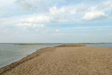 The coastal line of a sandy beach by the Baltic Sea on Sobieszewo island, Poland. There is a small pond separated from the sea by sand dunes. A bit of overcast. Few tress in the back. Calmness.