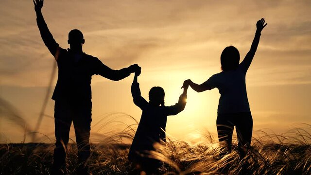 Family teamwork. People in park raise their hands up. Silhouette young team in park. High grass. Teamwork at sunset. Family raises their hands up. Silhouette of a family in grass in park