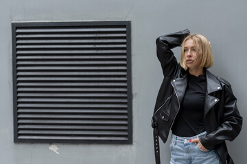 Beautiful blonde model posing in fashionable style near a gray wall