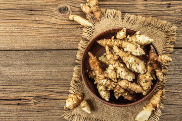 Raw Jerusalem artichoke in a bowl on wooden boards background