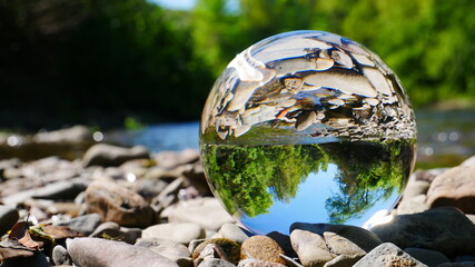 lensball photo with reflection of a river with a stone bank and a green spring forest in a crystal...