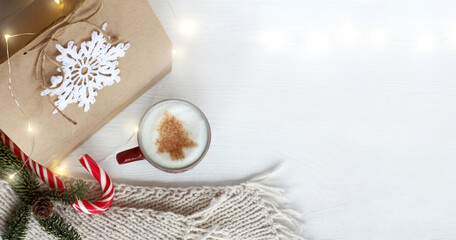 gift, scarf, cup of coffee with a pattern of a Christmas tree on a table with garland lights top view. warming atmosphere of winter festive morning