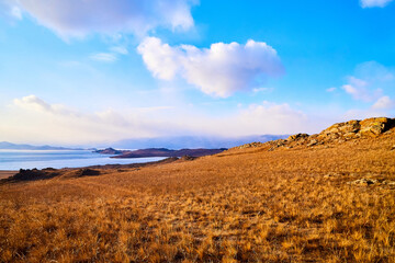 Nature landscape with golden field, wather, hills and blue sky with white clouds in a day or a evening