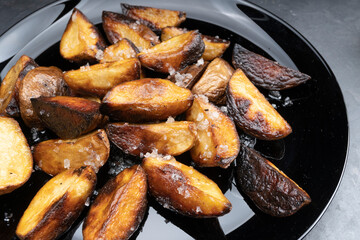 Rustic fried potatoes on a black dish on the table, top view