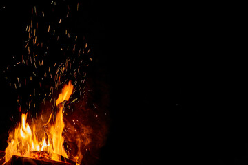Fire or campfire lit. High flames with sparks. Half of the image in black with space for writing....