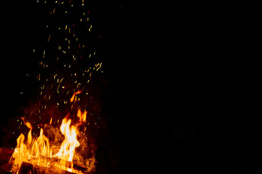 Fire or campfire lit. High flames with sparks. Half of the image in black with space for writing. Photo for design, wallpaper, text.