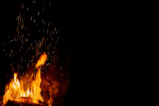 Fire or campfire lit. High flames with sparks. Half of the image in black with space for writing. Photo for design, wallpaper, text.