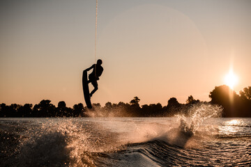 beautiful view of dark silhouette of active male rider holds rope and making extreme jump on...