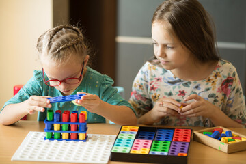 A girl with Down syndrome is engaged in elementary mathematics with her older sister, having fun...