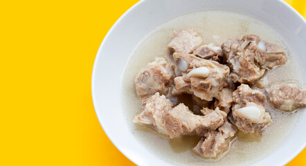 Boiled pork ribs in white bowl on yellow background.