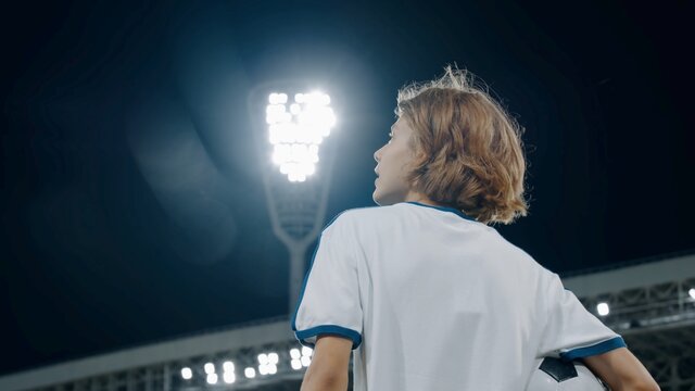 Portarit of Caucasian pre teen kid boy entering the field of huge soccer stadium, holding a ball, dreaming of becoming professional player, soccer star