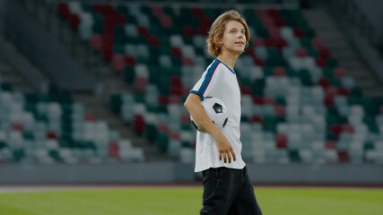 Portarit of Caucasian pre teen kid boy entering the field of huge soccer stadium, holding a ball, dreaming of becoming professional player, soccer star