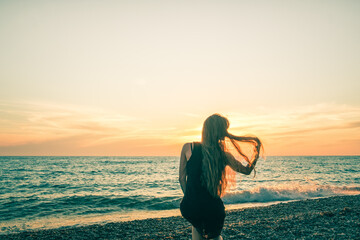 Silhouette of a slender girl on a sunset background. The sun falls over the horizon of the sea. Evening, light breeze and a young lady on the shore. Hair flutters. Russia. Day. Summer.