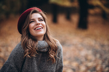 Portrait of a joyful young woman enjoying in the autumn park. beautiful blonde girl in autumn red beret and gray sweater. Relax in nature